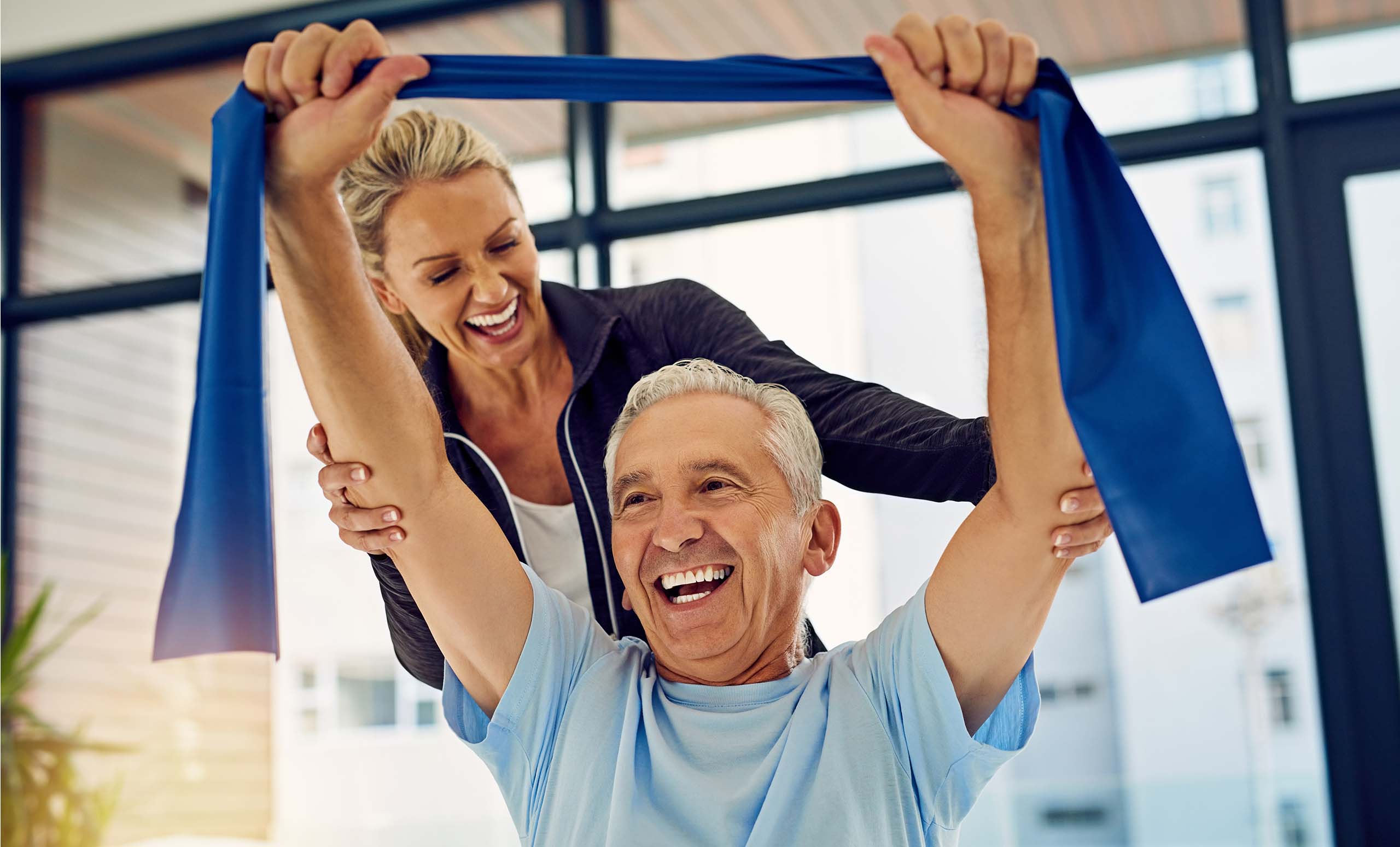 Picture of a man doing shoulder exercises with stretch band, supervised by a physical therapist.