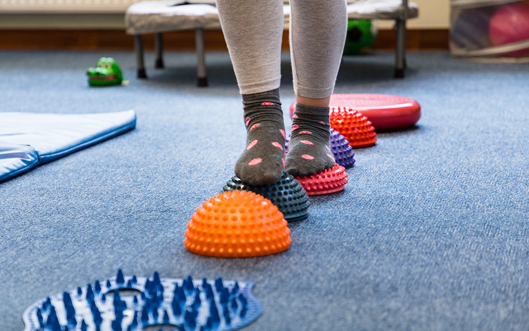 Pictured is a child walking on a sensory mat and pillows.